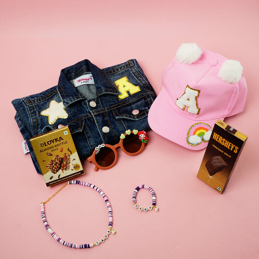 Collection of denim jacket, pink cap with 'A' design, sunglasses, and candy bars on a pink background